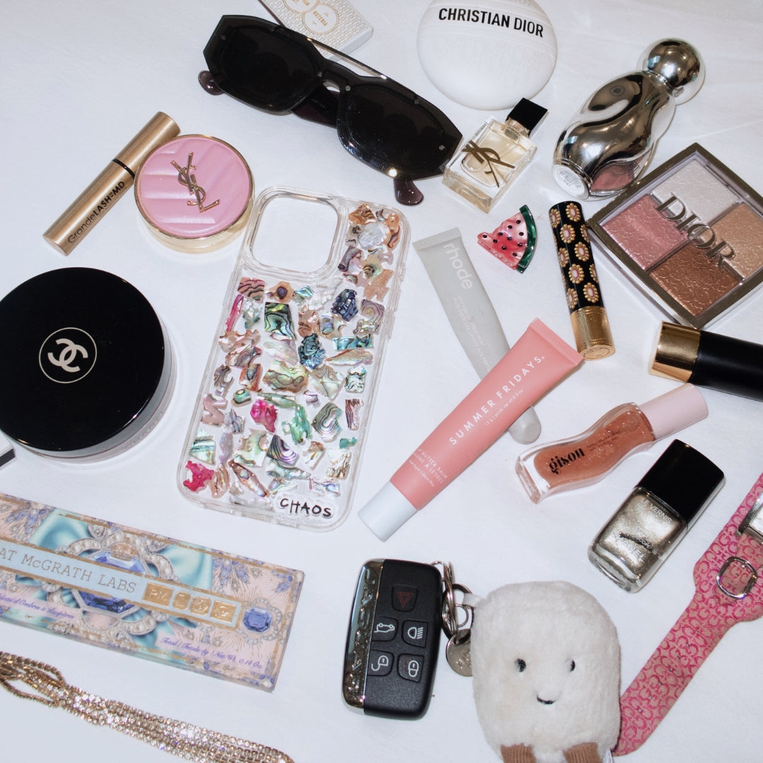 Chaos Cases Abalone Shell iPhone Case styled in flat lay with designer makeup, perfume, sunglasses, and accessories